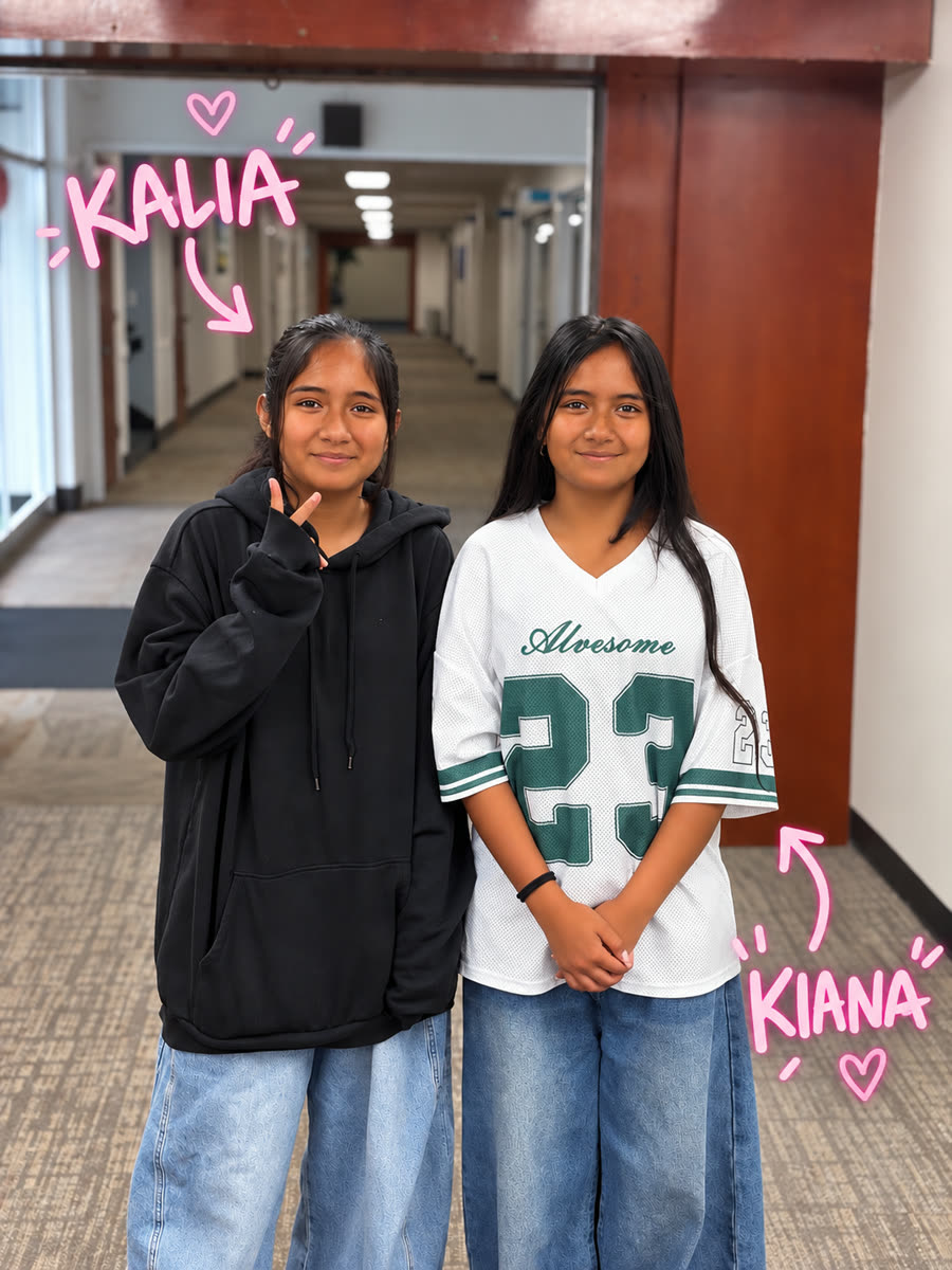 Twin sisters Kalia and Kiana Pene standing side by side in a hallway, with their names drawn in pink